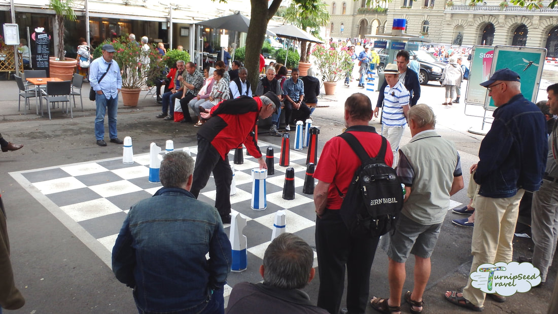 Men gather in the public square to watch a game of chess.