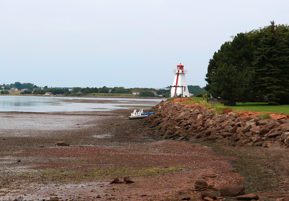 Small white lighthouse with red trim side on a rocky shore at the end of a public park at low tide