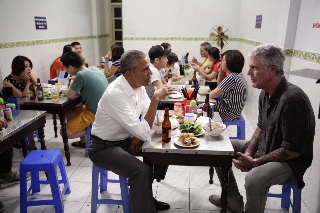 President Obama and Anthony Bourdain sit at a small table with blue chairs in a crowded Hanoi cafe.Picture