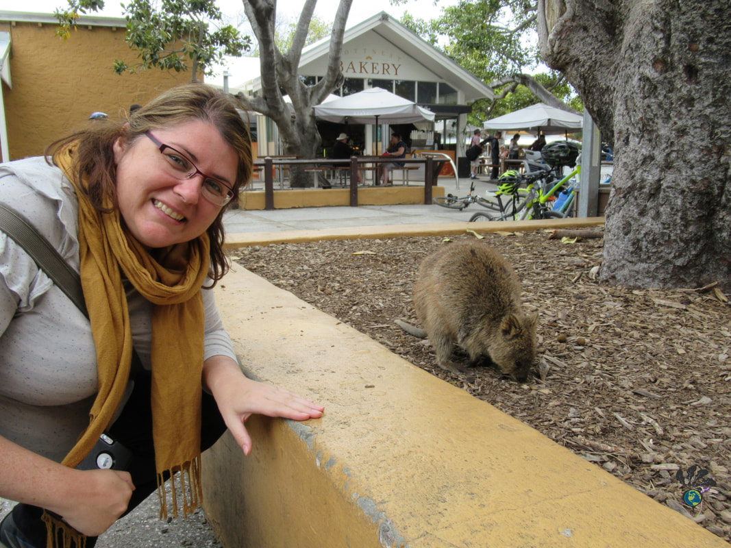 Vanessa poses next to a quokka while wearing a yellow scarf and grey shirt
