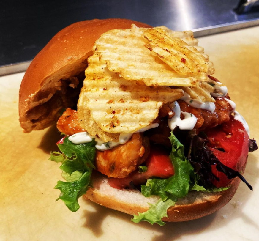 Sandwich bun topped with chips, creamy sauce, chicken, and tomatoesPicture
