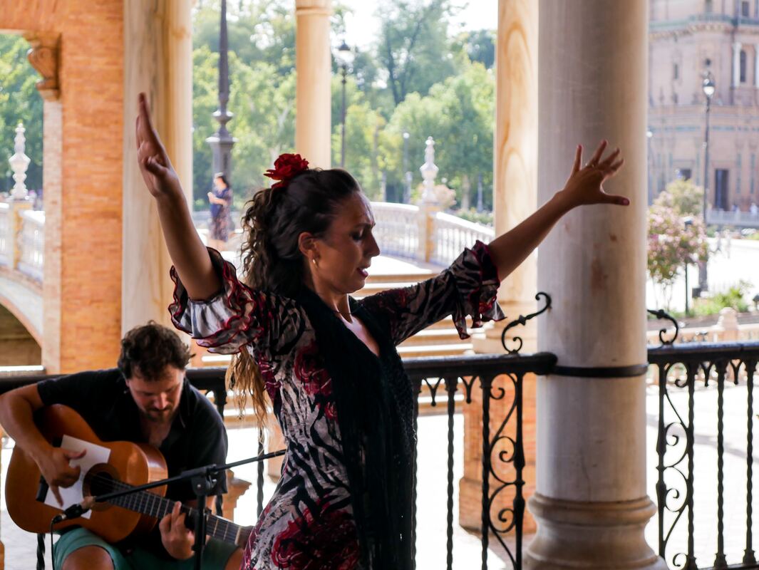 A female flamenco dancer performs while a man plays guitar in the background in an outdoor space 
