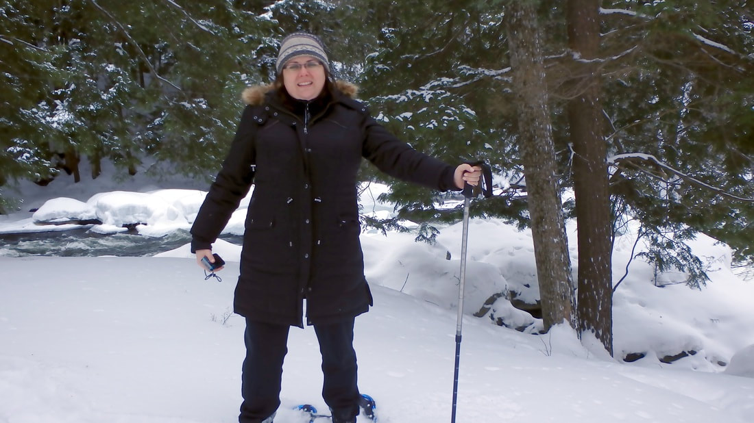 Vanessa snowshoes while wearing a large black coat