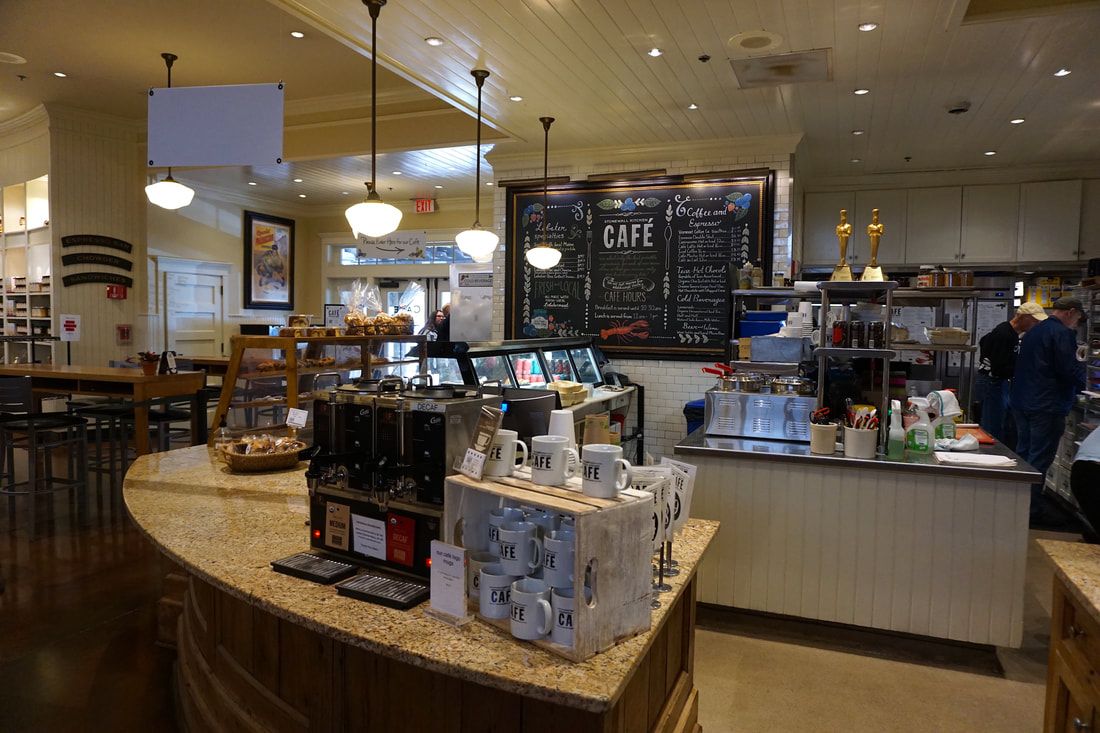 Inside of the cafe showing the counter, mugs, and people preparing food in the back