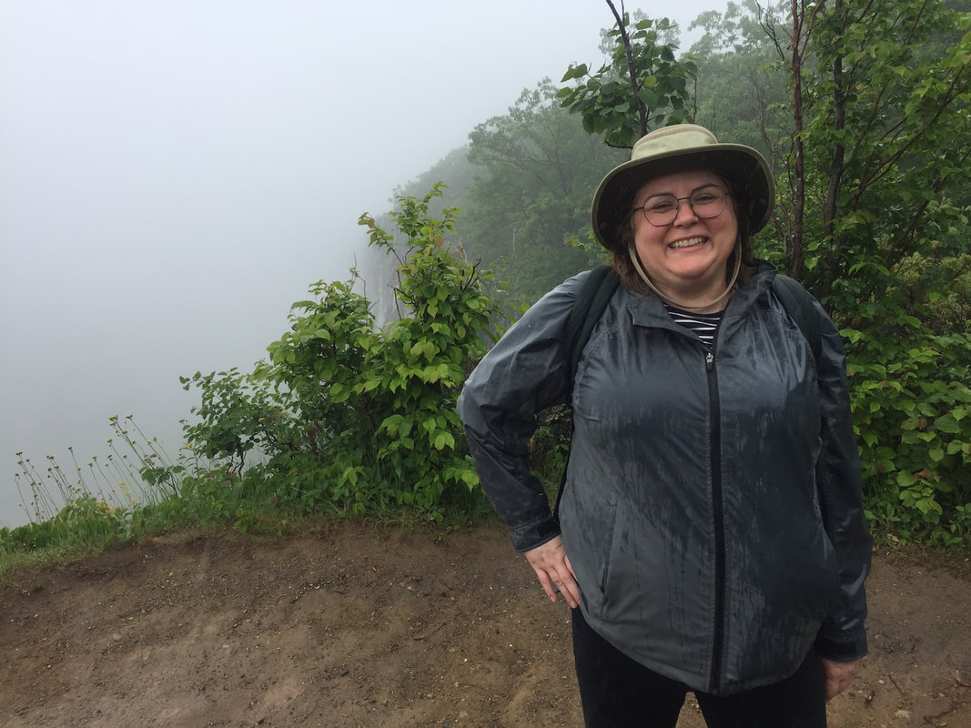 Vanessa standing at the summit of the Cup and Saucer trail, wearing a grey rain coat in the rain and fog.
