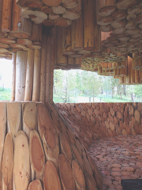 An outdoor covered concert space made from hundreds of pieces of cut logs of different heights