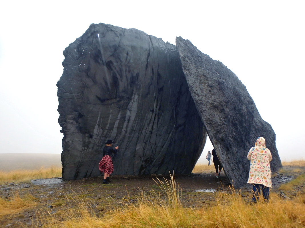 Tippet Rise music, art, adventure: Several people are dwarfed by the large grey stone columns of a piece of outdoor art.