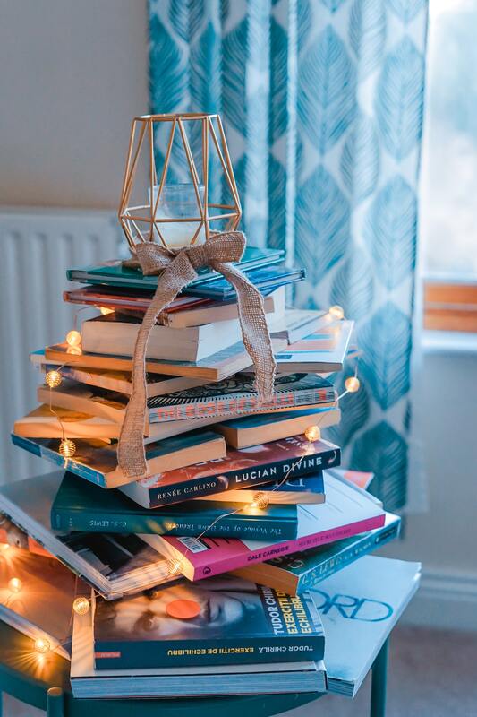 A stack of books sits arranged with a candle on top and mini twinkle lights cascading down.