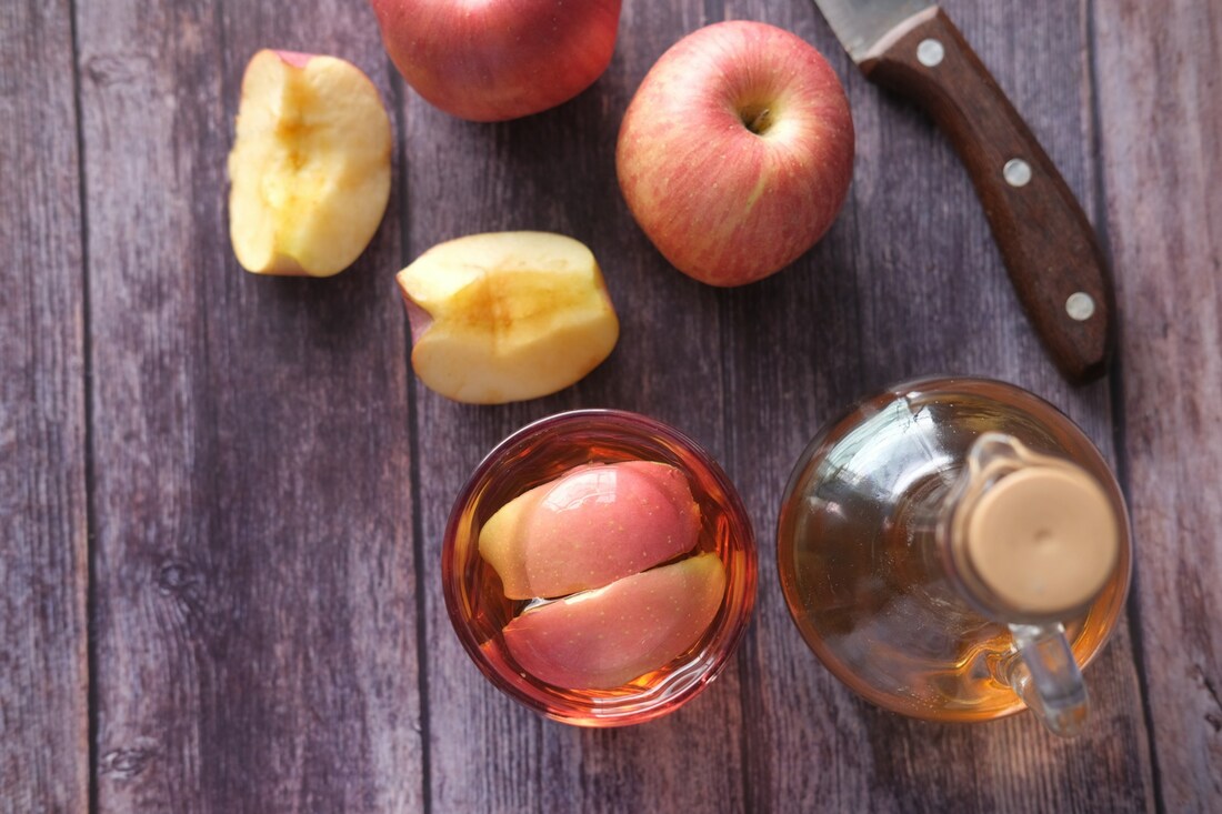 Slices of apple on a brown wooden table with a knife and bottle of cider on the side.Picture
