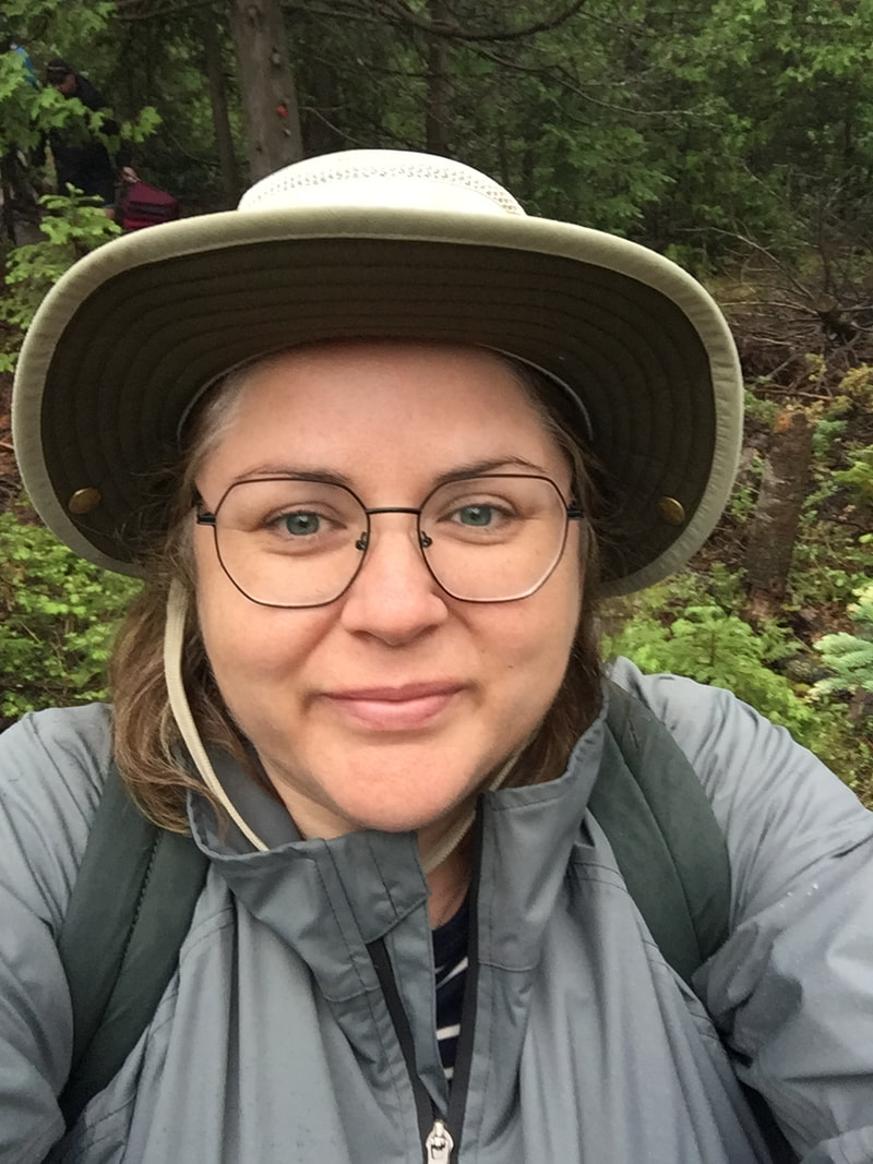 Vanessa takes a selfie in a grey rain coat and beige hat.