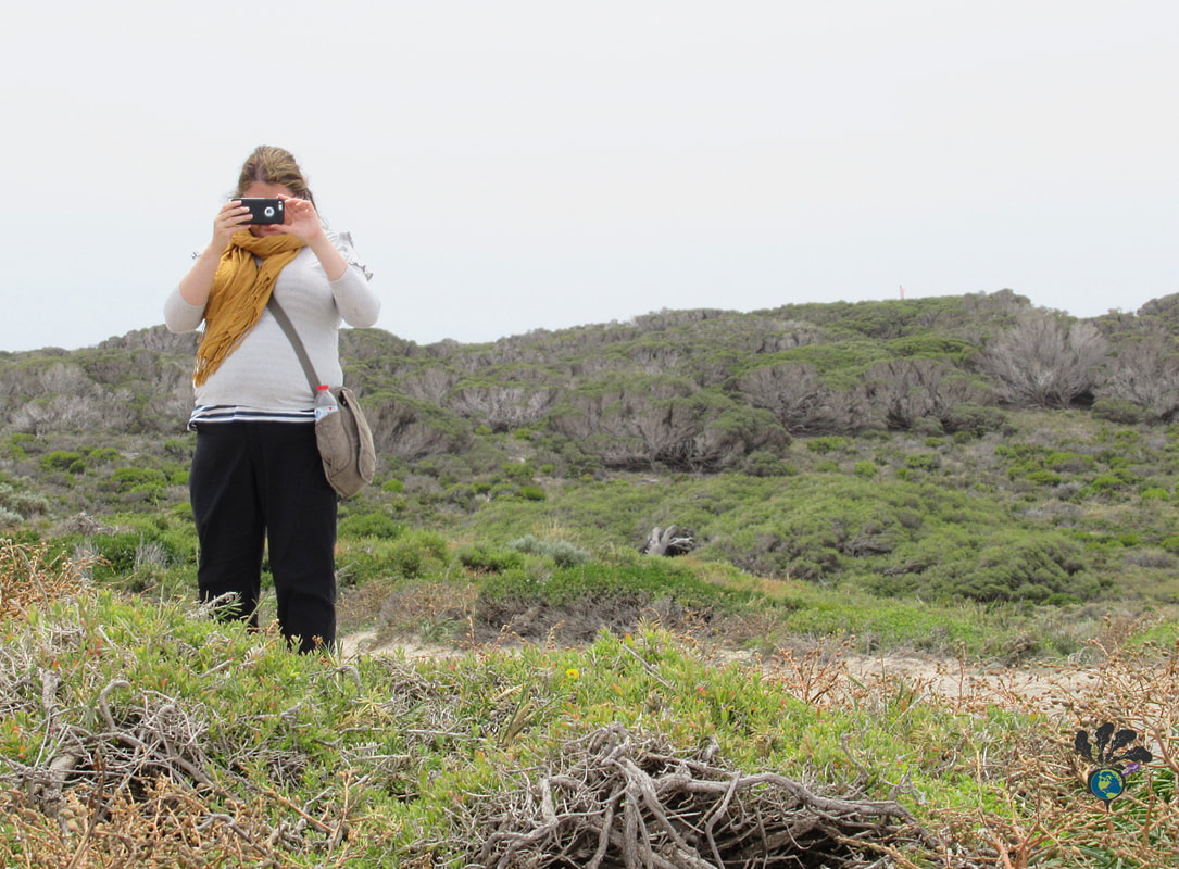 Vanessa takes a photo of the landscape while wearing black pants, grey shirt, and yellow scarfPicture