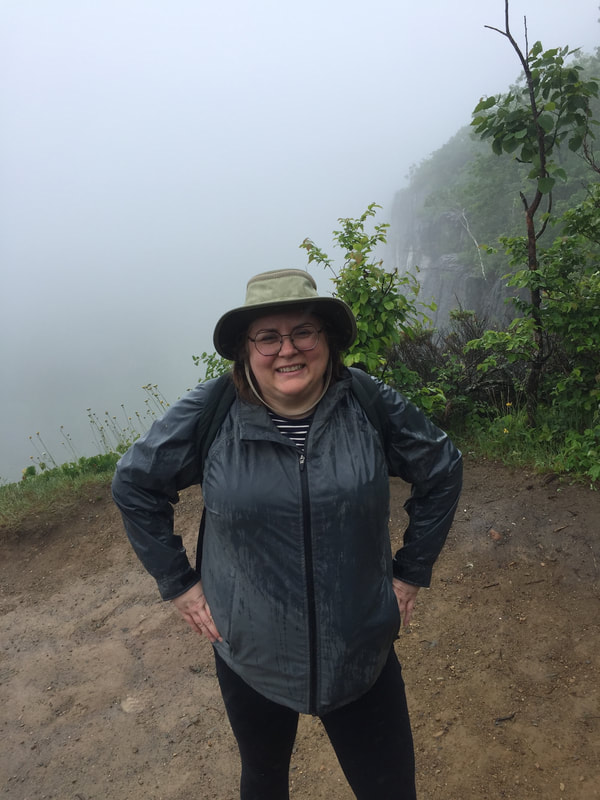 Vanessa poses in the rain at the summit of the trail, with a misty background.