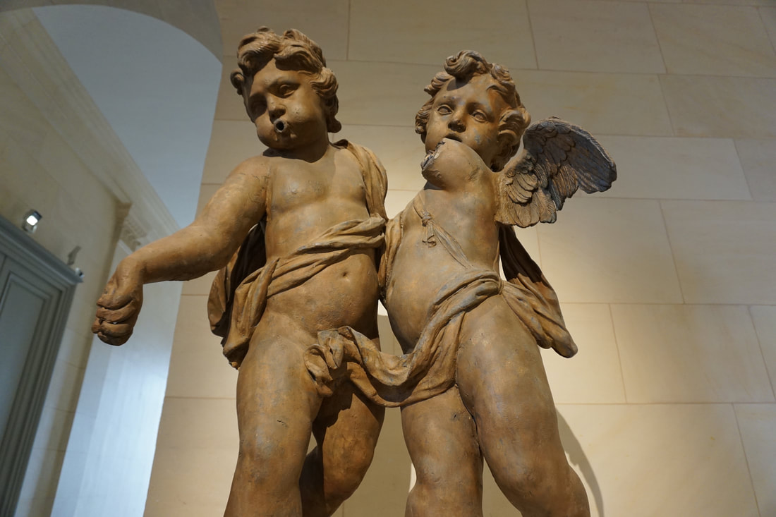 Statue of two bronze coloured baby angels in front of a white marble wall