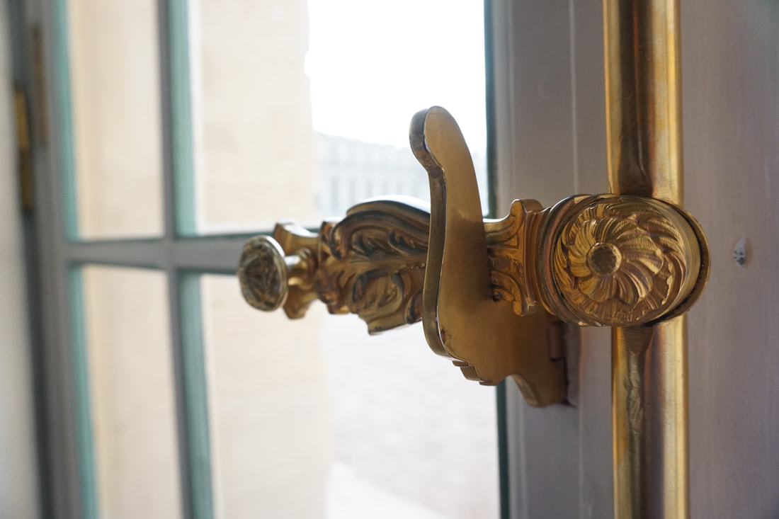 Close up of an ornate gold window latch and a window in the background with a light blue frame.