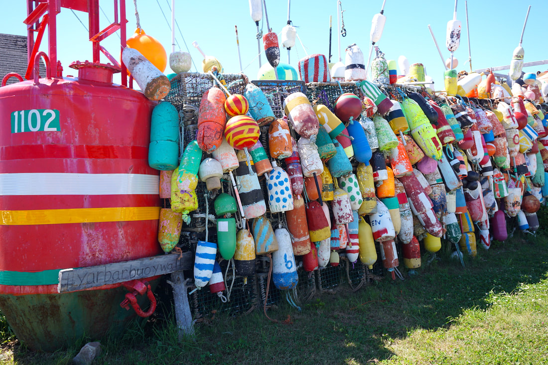 A wall of colourful buoy in all imaginable shades an patterns, at least five high and thirty wide, plus a large red commercial buoy in the foreground.