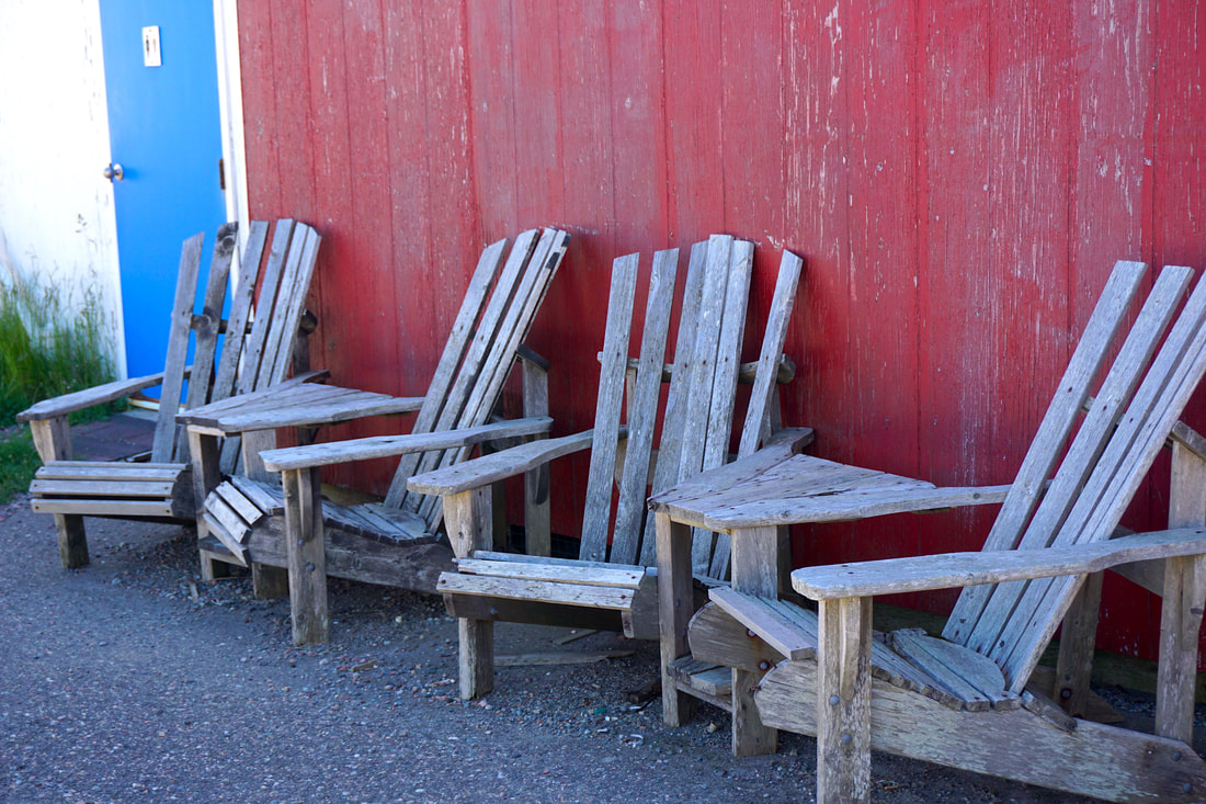 Best things to do in Yarmouth: Four weather beaten grey wood chairs rest in front of a red painted wood wall.