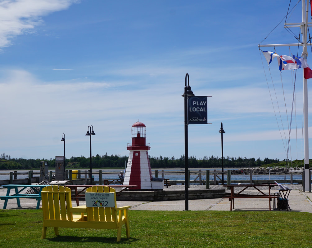 Red and white stripped mini lighthouse at the harbour, plus yellow chairs and assorted picnic tables