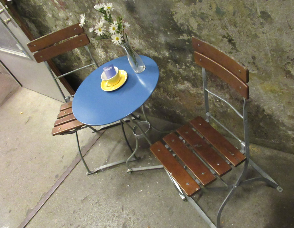 Small blue cafe table set up outside with two small wooden folding chairs