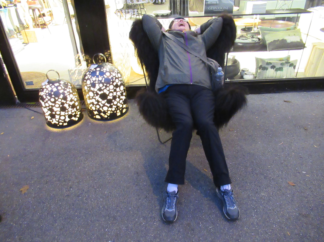 Vanessa sits back and laughs on a black chair covered in faux fur outside a design store.
